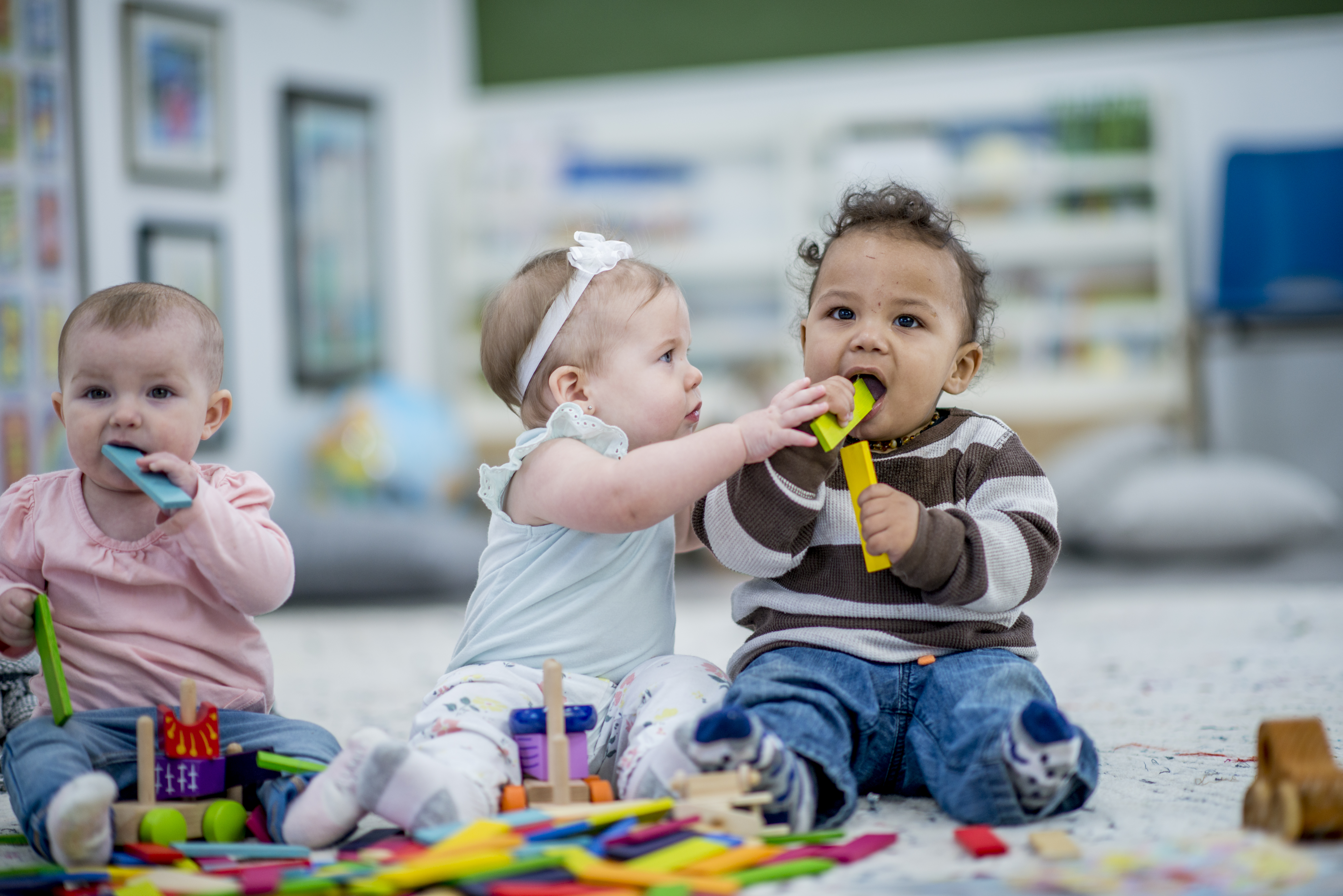 an infant reaches for a toy that a fellow infant is chewing