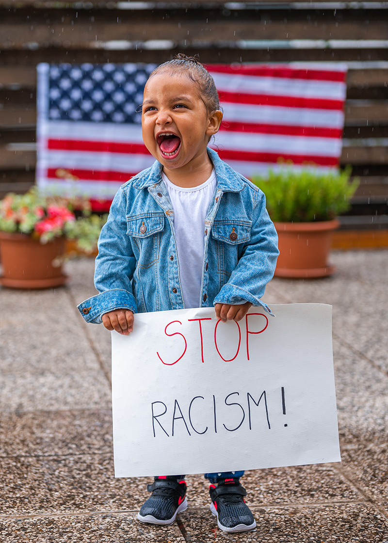 Gleeful toddler holds 'stop racism!' sign with U.S.A. flag in background