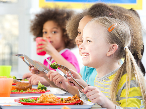 several children sitting at a table smiling and eating during mealtime