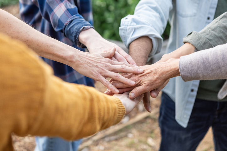 multigenerational team huddle - hands placed together in a circle in team unity