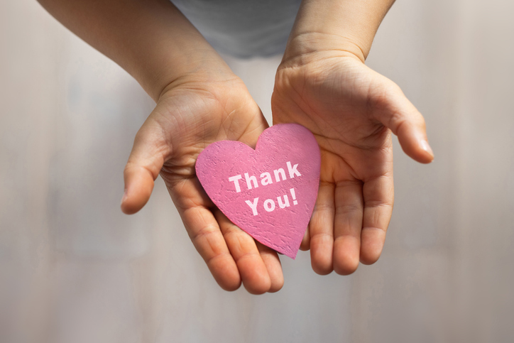 Open hands holding a heart-shaped card that reads “Thank you!”